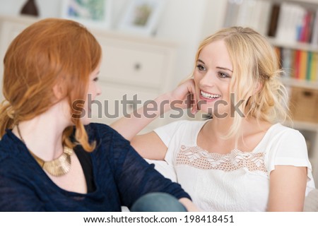 Two attractive women chatting as they relax at home sitting on a comfortable sofa in the living room laughing and smiling