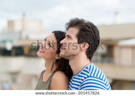 Profile view of an attractive young couple standing close together watching something up in the sky