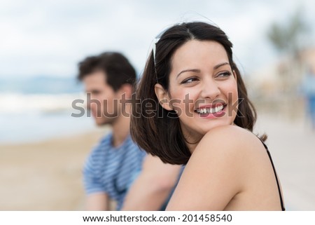 Beautiful young woman at the beach smiling as she looks back over her shoulder at something off frame