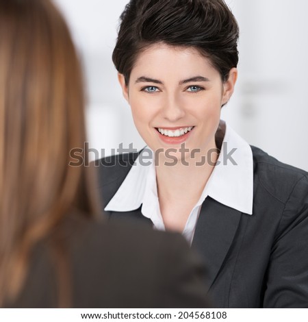View over the shoulder of a colleague of the face of a beautiful friendly businesswoman looking at the camera with a smile