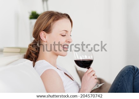 Beautiful woman appreciating a glass of red wine smiling with satisfaction as she looks down at the glass tilted in her hands while enjoying a quiet evening at home