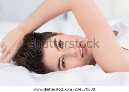 Beautiful young woman relaxing in bed lying on her back with her face turned to the camera with a serious expression and parted lips as she enjoys a lazy day