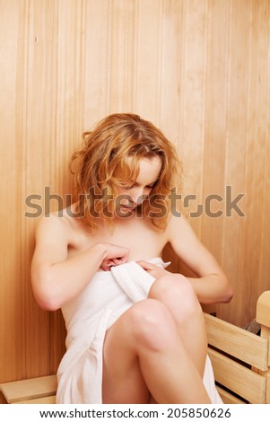 Young woman wrapping herself in a fresh clean white towel as she settles down to enjoy an invigorating healthy sauna
