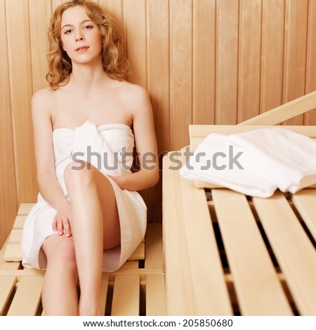 Relaxed young woman in a sauna bath sitting on a wooden bench leaning against the wall looking at the camera with a sleepy expression