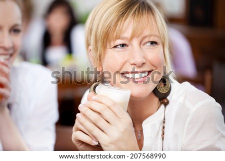 Happy young woman with friend holding coffee cup while looking away in cafe
