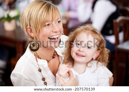 Laughing vivacious young mother with her beautiful daughter cradled in her arms looking at the camera with a cute smile