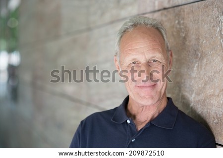 Smiling attractive grey-haired man standing alongside a receding exterior wall looking at the camera with copyspace