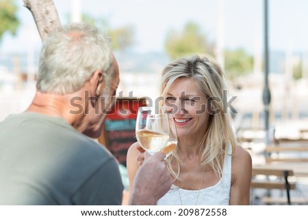 Happy mature couple toasting each other as they celebrate a summer vacation with white wine as they sit at an outdoor table at an open-air restaurant
