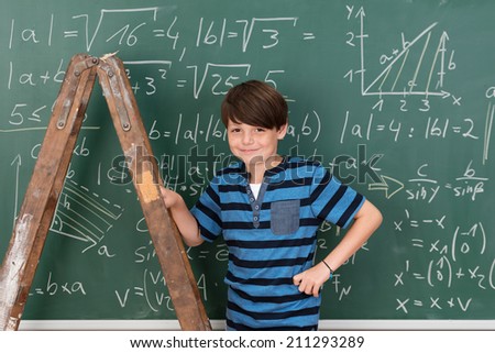 Confident smiling young boy prodigy in school during mathematics class using a stepladder to reach complex equations on the chalkboard