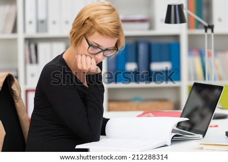 Businesswoman hard at work in the office sitting at her desk reading through paperwork with her chin resting on her hand