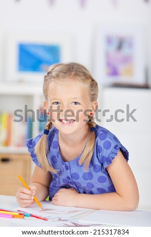 Little girl with blond hair drawing with color pencil on table at home