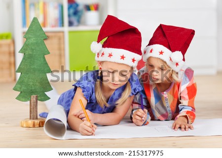 Two kids with santa hats writing wishlist while lying on the floor