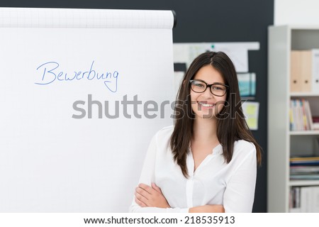 Smiling confident young businesswoman doing a presentation standing alongside a flip chart in the office with folded arms