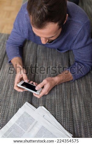 High angle view of a man sending a text message on his smartphone navigating the touch screen with his thumb as he sits at a wooden table