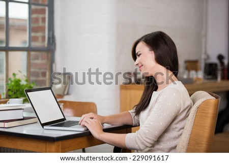 Pretty woman sitting at a table in her apartment working at a laptop smiling as she reads the screen
