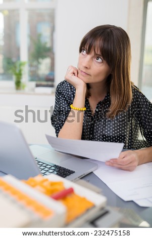 Middle Age Office Woman Thinking Something of What to Write on White Paper with Laptop on the Side. Captured Office Indoor.