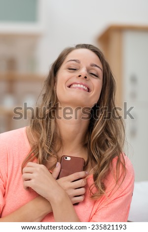 Young woman romanticizing after a phone call clutching her mobile to her chest and looking up with her eyes closed and a dreamy look of pleasure