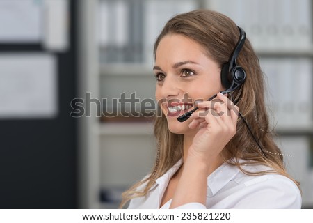 Attractive young client services assistant with a lovely smile listening to a customer on her headset as she offers assistance
