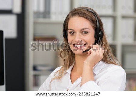 Friendly attractive call center operator smiling at the camera with a lovely friendly call as she takes a call on her headset in the office