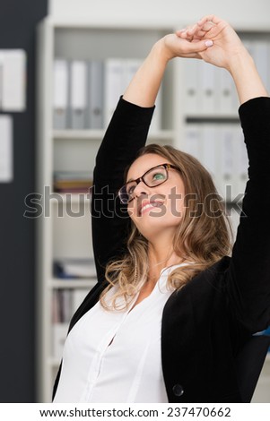 Young businesswoman relaxing at work stretching her hands above her head with a contented smile and thoughtful expression