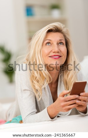 Middle-aged woman lying thinking on a couch in the living room staring up into the air with a tablet computer in her hands