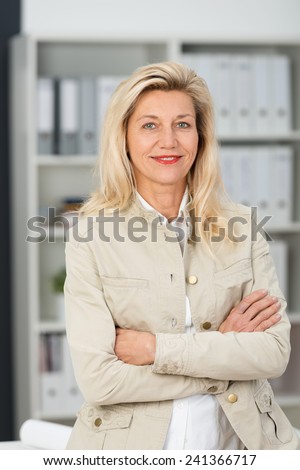 Self-assured friendly attractive middle-aged businesswoman in a stylish jacket standing with folded arms smiling at the camera
