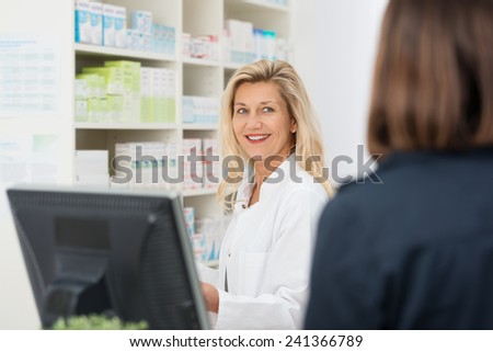 Attractive smiling female pharmacist assisting a patient in the pharmacy, over the shoulder view to the pharmacist