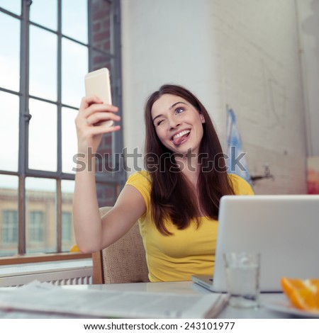 Playful young woman posing for a selfie on her mobile phone pulling a face winking and sticking out her tongue