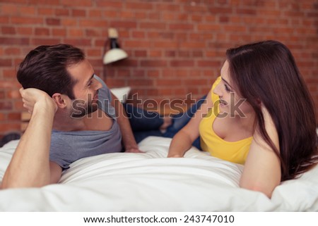 Young couple spending a relaxing lazy day lying chatting and laughing on the bed facing each other