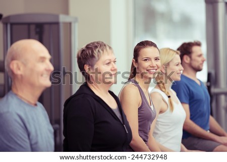 Group of three diverse women standing in a gym class with two men with focus to an elderly, and young friendly smiling woman, in the centre in a healthy lifestyle concept