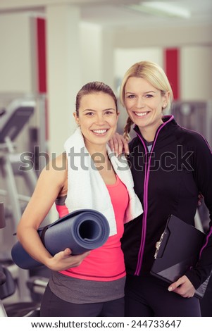 Close up Fit Young Woman with Mat Posing with her Female Gym Instructor at the Fitness Gym.