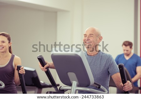 Fit handsome elderly balding man working out in a gym on their equipment with a female friend smiling happily in enjoyment in a healthy lifestyle concept