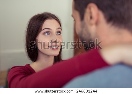 Loving young woman looking at her husband with a smile as she stands with her arms around his neck, view over his shoulder of her face