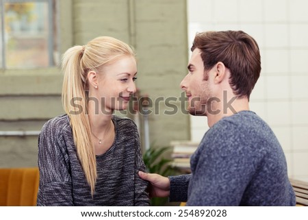 Loving couple sharing a tender moment together as they sit on a sofa in the living room looking deeply into each others eyes with a smile of affection