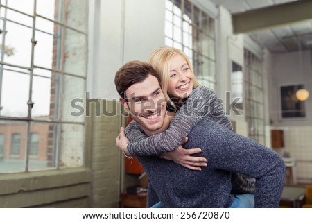 Playful loving couple enjoying a piggy back ride inside their spacious apartment with the husband giving his smiling wife a lift on his back