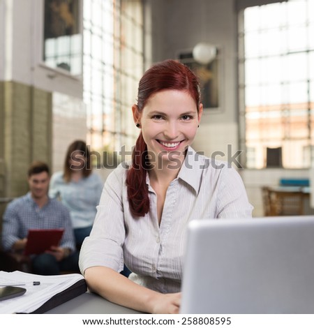 Close up Pretty Smiling Woman with Long Burgundy Hair in Off White Blouse Sitting at Worktable with Laptop Computer