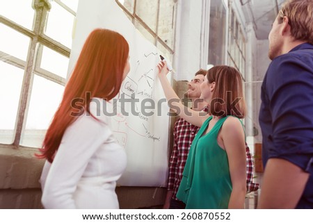 Young woman giving a presentation to her business colleagues or team standing drawing a flow chart on a flip chart in the office