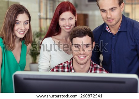 Successful business team working around a computer monitor grouped around the seated team leader smiling as they read the screen