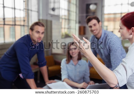Young business team of diverse men and women listening to their team leader as she explains a point gesturing with her hand, focus to her arm and side of her face