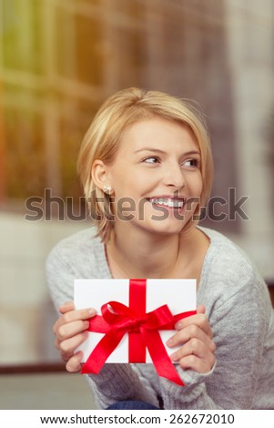 Joyful woman holding a Valentines or birthday gift tied with a large red bow looking off to the side with a beaming smile