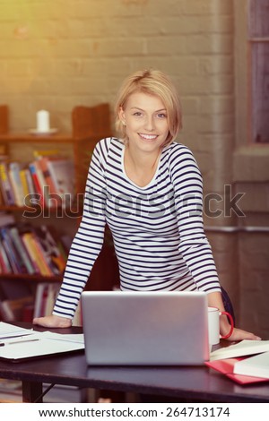 Smiling Pretty Blond Woman in Black and White Stripe Shirt Leaning on the Table with Laptop While Looking at the Camera.