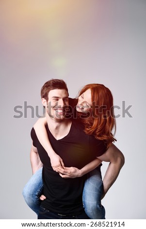 Portrait of a Happy Sweethearts - Young Handsome Man Carrying his Girlfriend on his Back at the Studio with Gray Background.