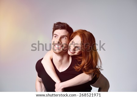 Close up Young Woman Embracing her Man While Looking to the Upper Left of the Frame. Captured in Studio with Gray Background and Light Coming From the Left.