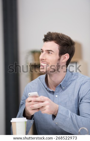 Excited handsome young man smiling with delight after reading a text message on his mobile phone