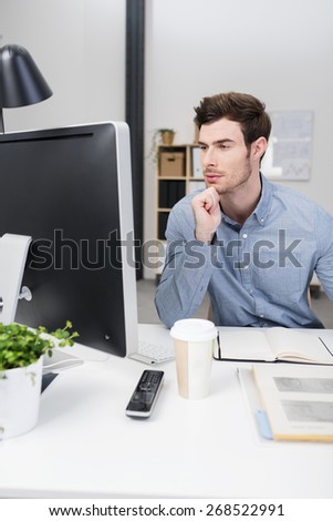 Businessman trying to solve a problem sitting at his desk staring at his computer screen with narrowed eyes and a thoughtful expression