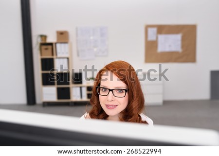 View over the top of the monitor of an attractive young woman working at her desktop in the office