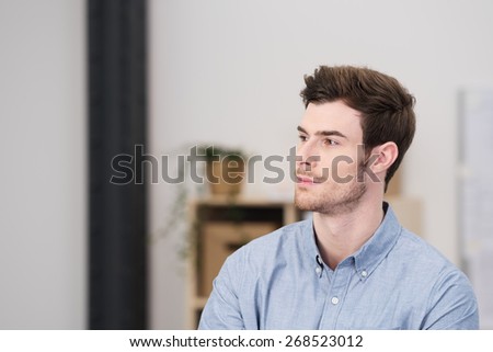 Serious pensive young man sitting at home staring off into space with a contemplative expression