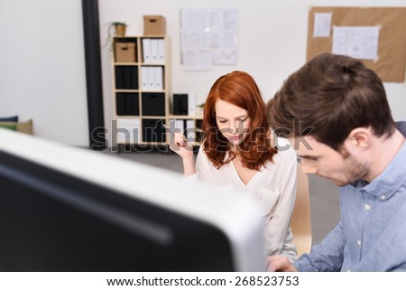 Man and woman working together in an office standing at a desktop computer discussing their business plan and strategy