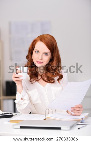 Close up Attractive Office Woman with Brown Hair Holding Report Papers and a Cup of Coffee While Looking at Camera with a Smile.