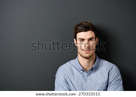 Close up Gorgeous Young Man Wearing Light Blue Gray Shirt Standing In Front of a Gray Wall with Copy Space at the Left Side.